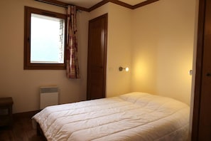 A bedroom with a bed, a window with curtains, a radiator, and a wall-mounted light.