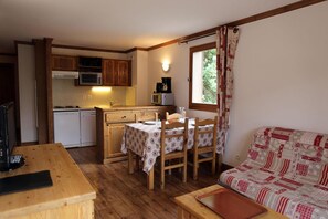 A compact kitchen with wooden cabinets, a dining table with chairs, and a window with curtains.