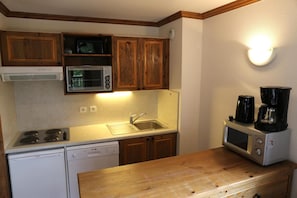 A compact kitchen with wooden cabinets, a microwave, a coffee maker, and a dishwasher.
