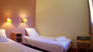 A hotel room with two single beds, a small bedside table, a nightstand, a radiator, and two wall-mounted lamps.