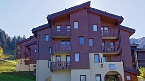 A multi-story wooden building with balconies, a central entrance, and a mountainous backdrop.