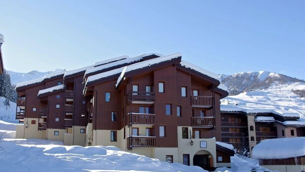 A multi-story hotel with balconies and a snowy mountain backdrop.