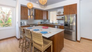 A modern kitchen with a central island, wooden cabinets, stainless steel appliances, and wicker chairs. - Casa Coral 2 Bedroom Home by RedAwning (Roatan)