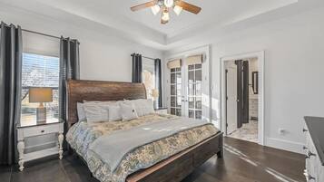 Une chambre avec un grand lit, un ventilateur de plafond et une vue sur l’extérieur par une fenêtre.