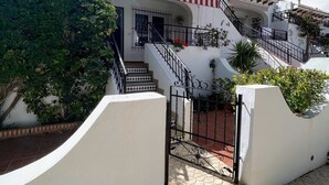 A white building with a red and white striped balcony, a staircase, and a gated entrance. - Botanical 2 Bedroom Bungalow with Com Pool VM33 (Orihuela)