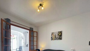 A bedroom with a bed, a nightstand, a chair, a painting, and a door leading to a balcony. - Botanical 2 Bedroom Bungalow with Com Pool VM33 (Orihuela)