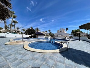 A pool area with multiple swimming pools, palm trees, and a clear blue sky.