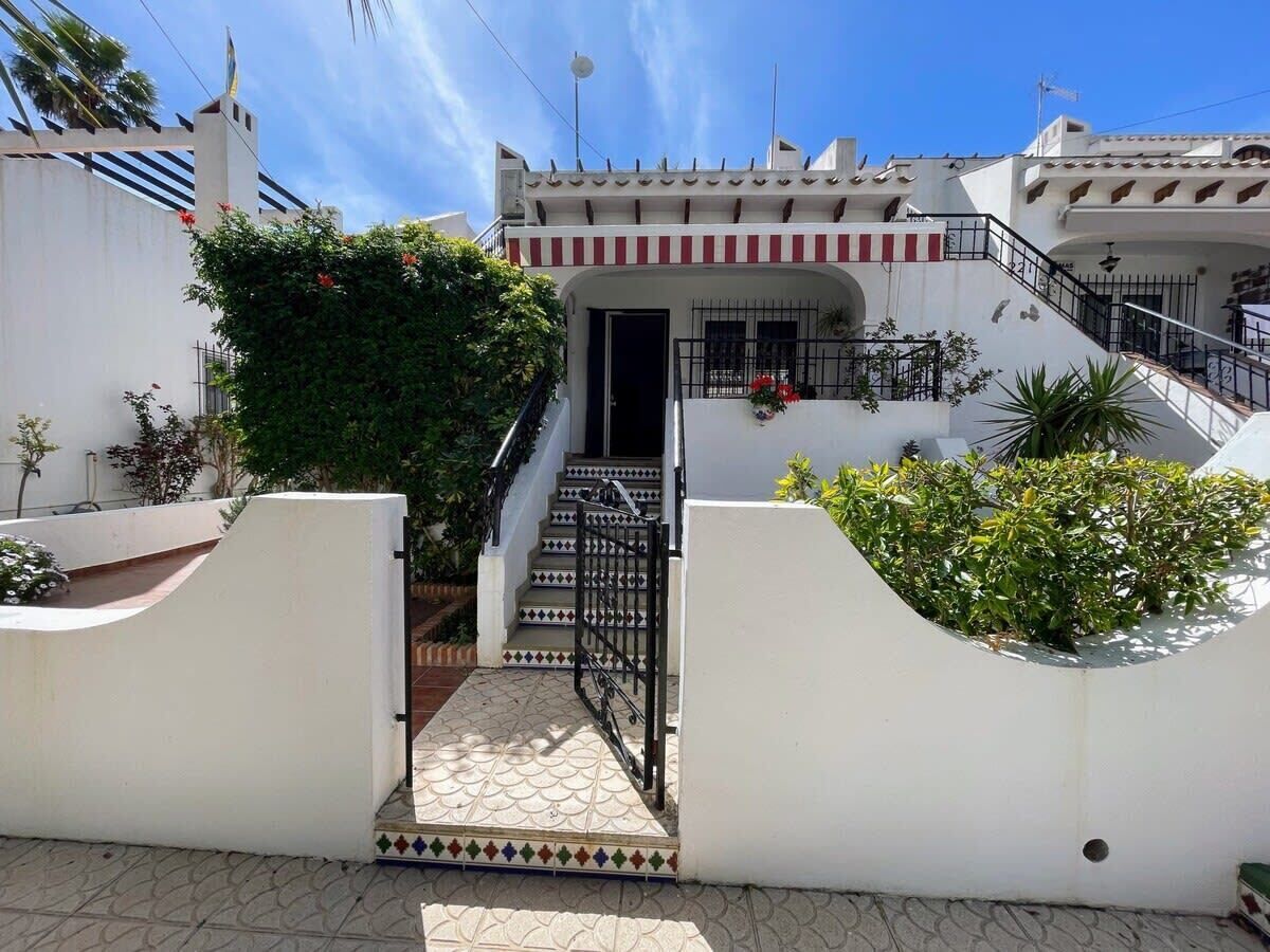A white building with a gated entrance, a staircase, and a small balcony with plants.