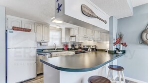 A modern kitchen with white cabinets, a large island with stools, a refrigerator, and a microwave. - N1 Amelia South 2 Bedroom Apts by RedAwning (Fernandina Beach)