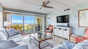 A spacious living area with a sofa, coffee table, and a television. There is a balcony with a view of the ocean. - N1 Amelia South 2 Bedroom Apts by RedAwning (Fernandina Beach)