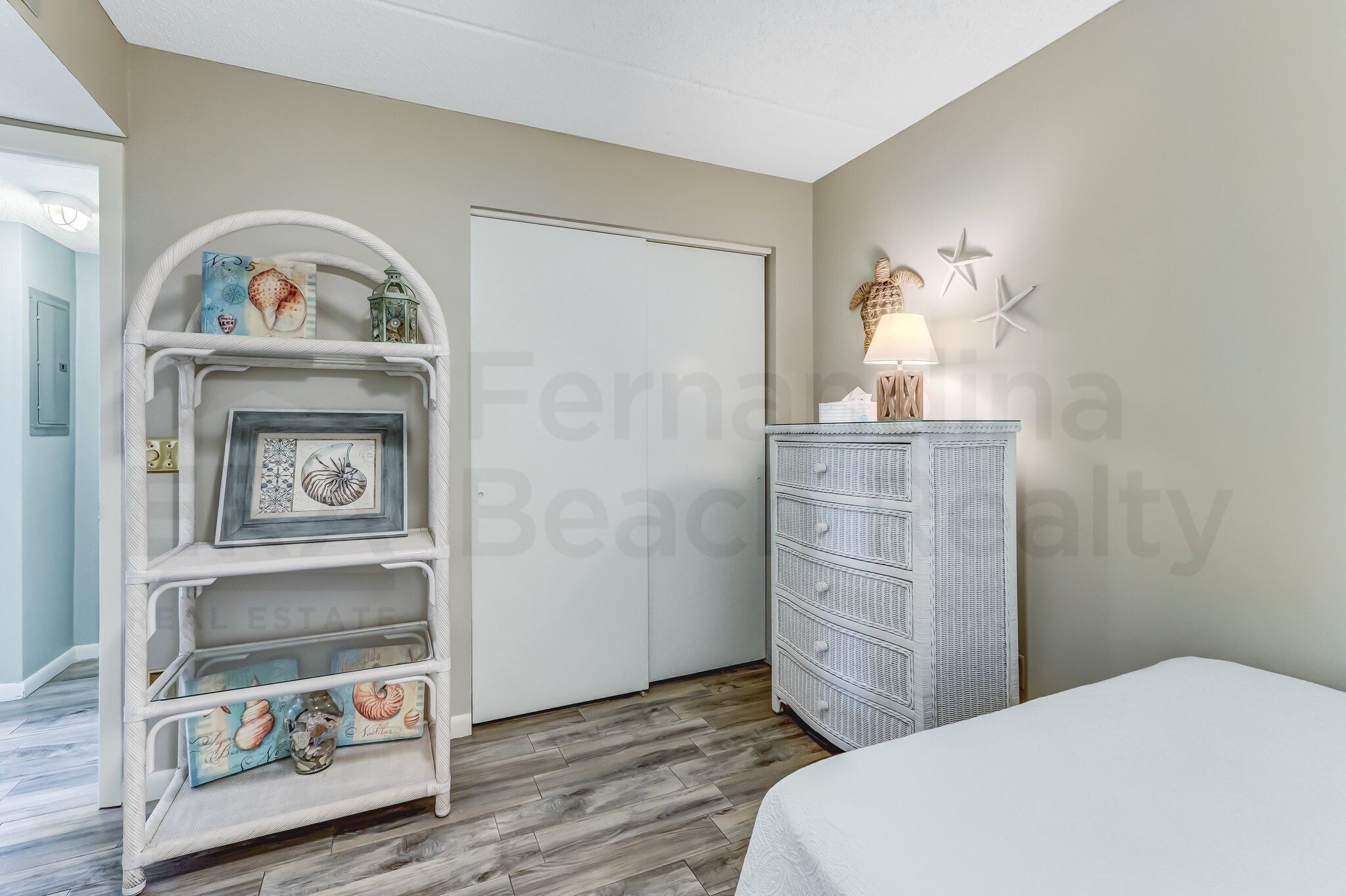A bedroom with a white bed, a white dresser with drawers, a white shelving unit with decorative items, a white door, and a starfish wall decoration.