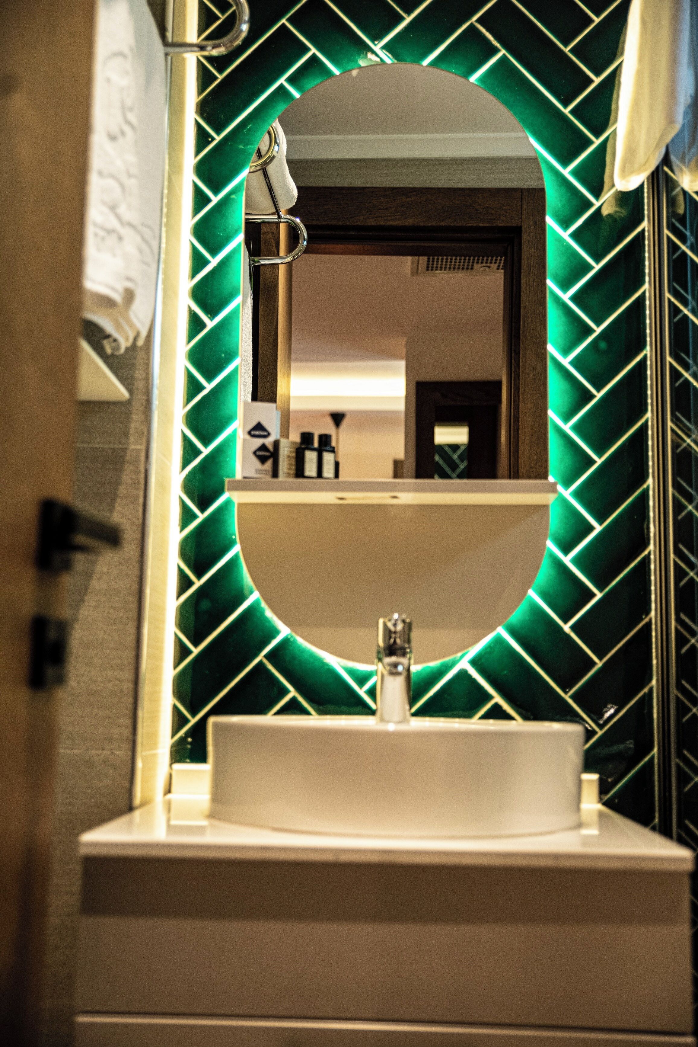 A bathroom with a white sink, a mirror, and a green patterned wall.