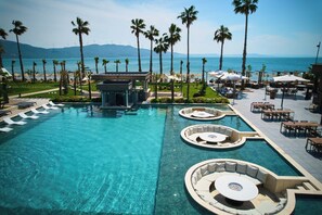 A resort pool area with multiple seating areas, palm trees, and a view of the sea. - Parmos Otel (Erdek)