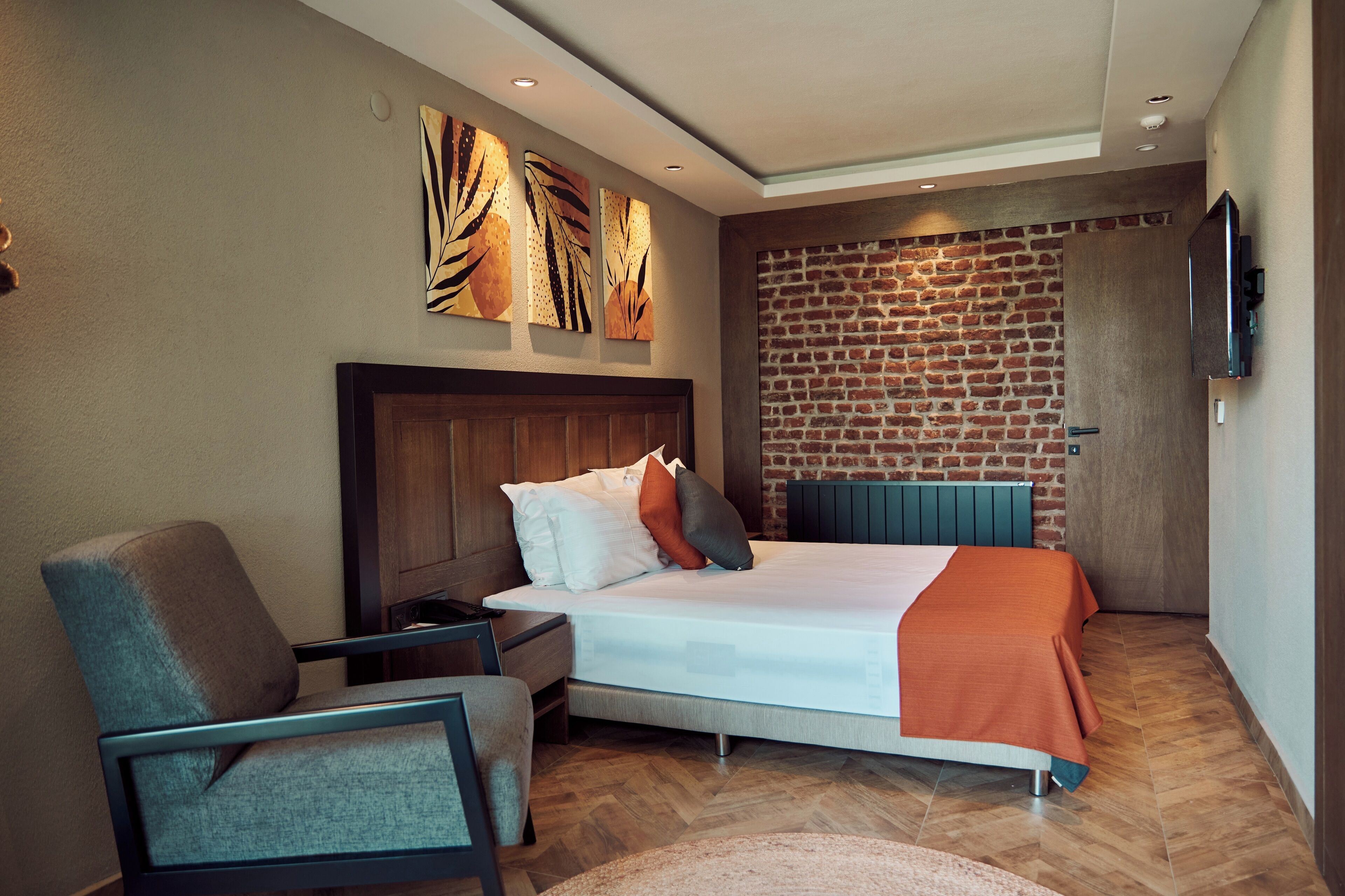 A modern hotel room with a brick accent wall, a large bed, a seating area, and artwork on the wall.
