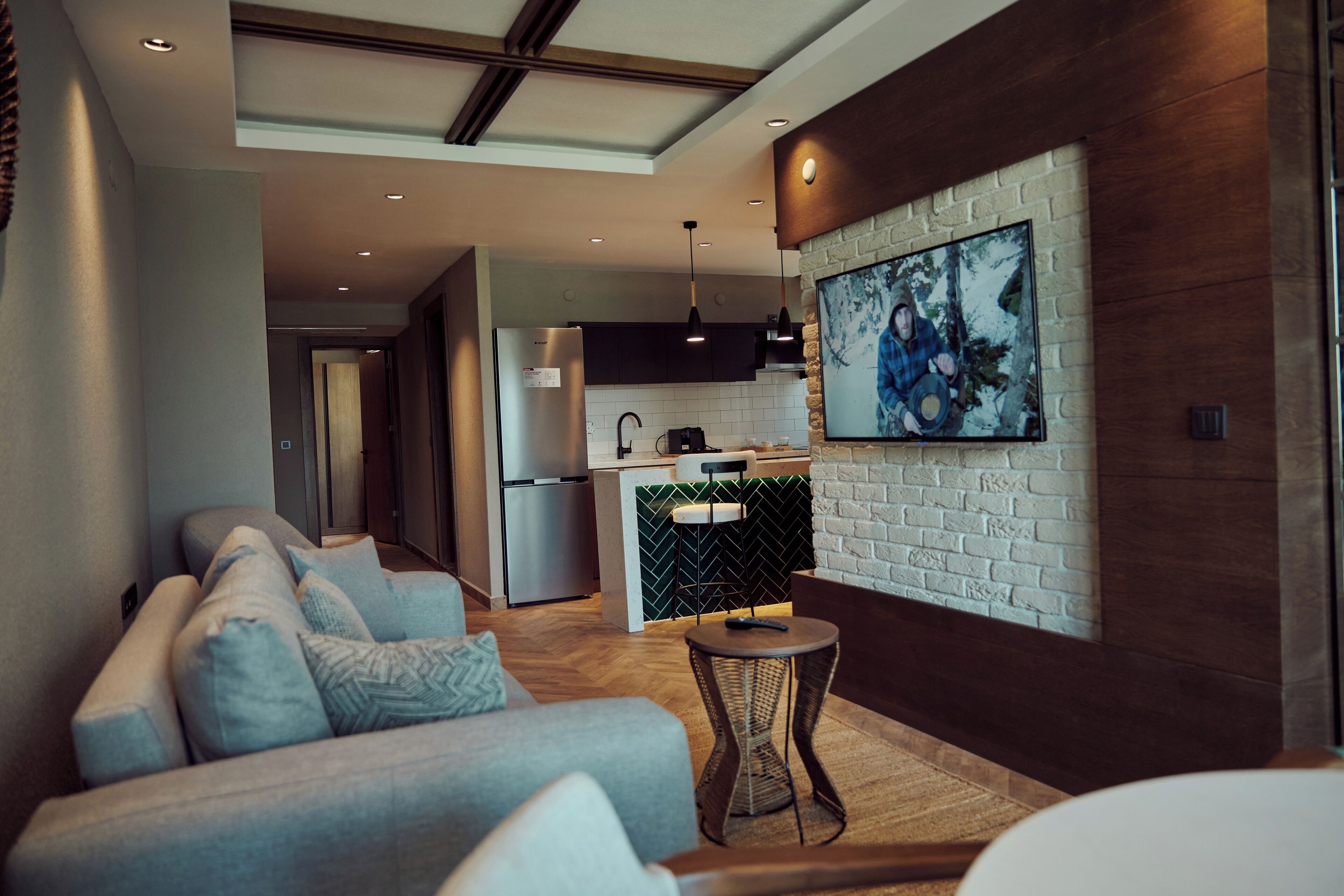 A modern living room with a sofa, a small round table, and a kitchen area with a refrigerator and a sink.