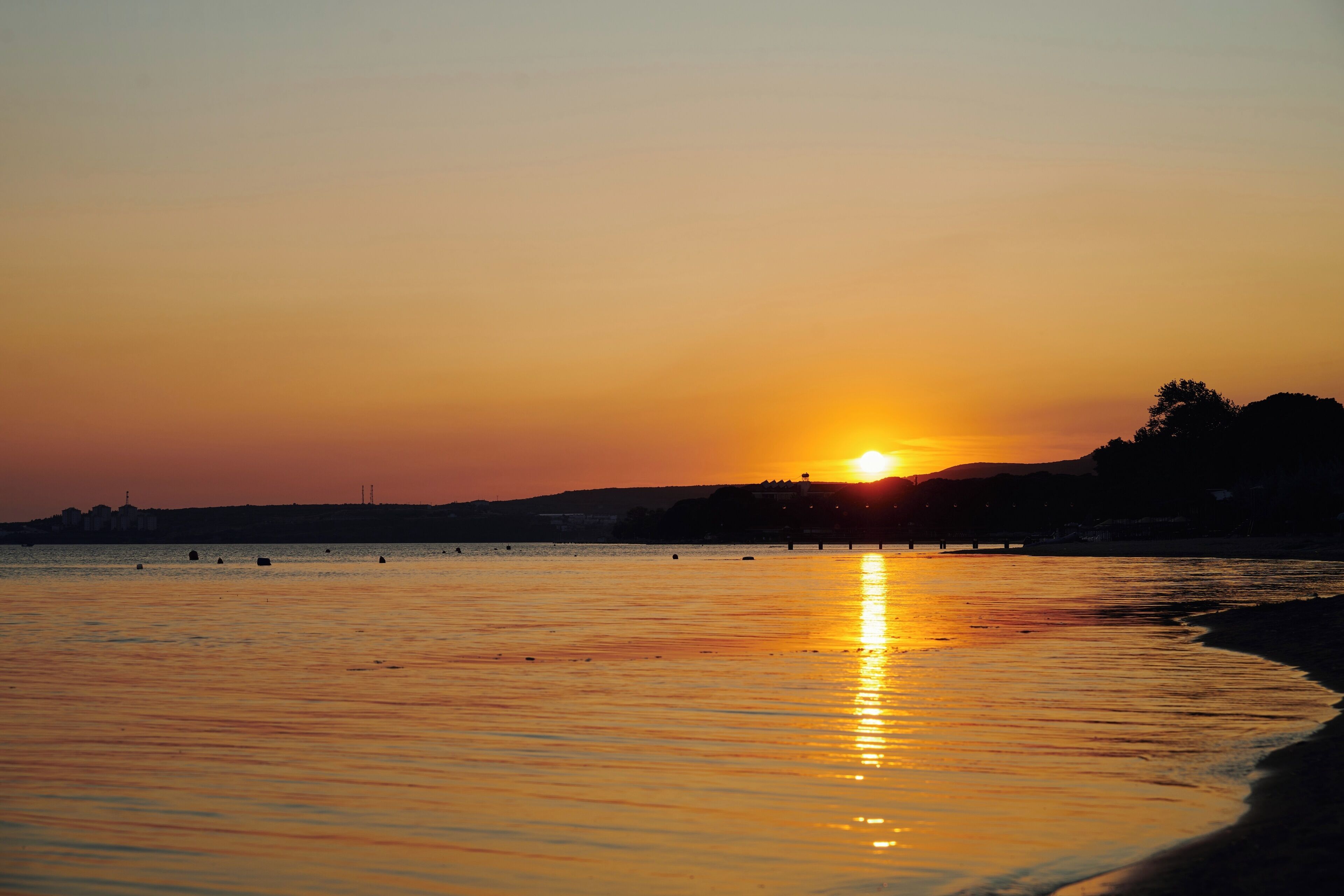 Um pôr do sol sobre águas calmas, com o contorno silhuetado de uma costa distante.