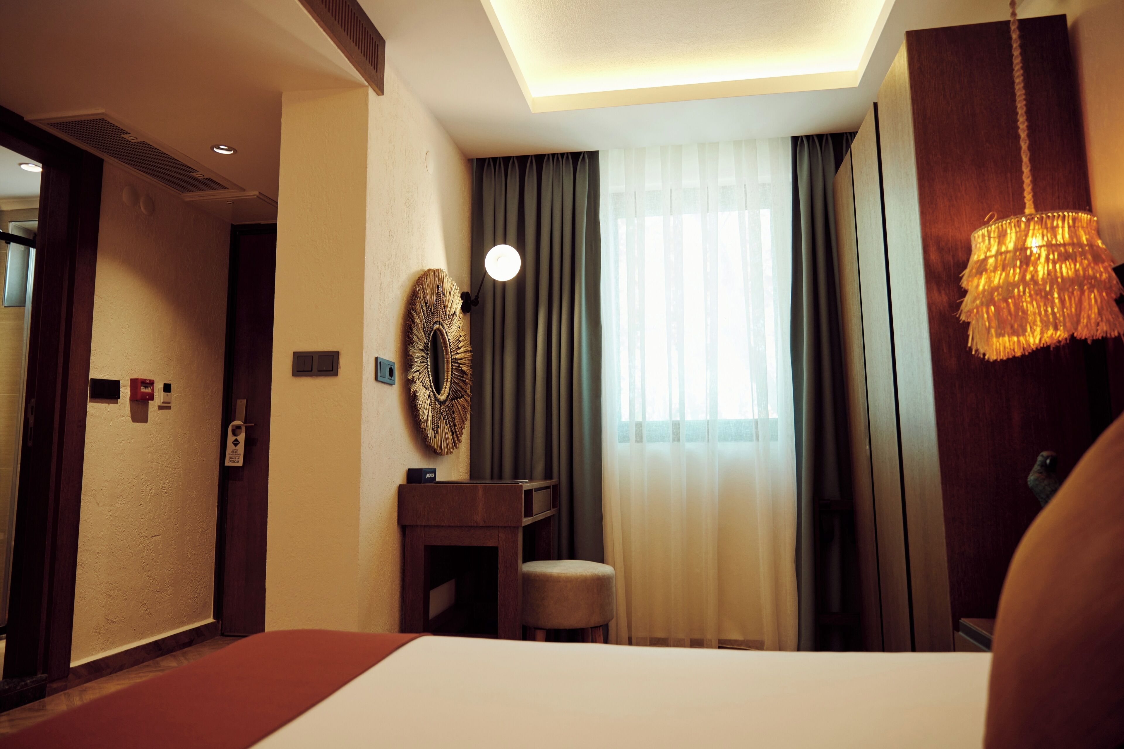 Una habitación de hotel con una cama, un escritorio, una silla, un espejo y una ventana con cortinas.