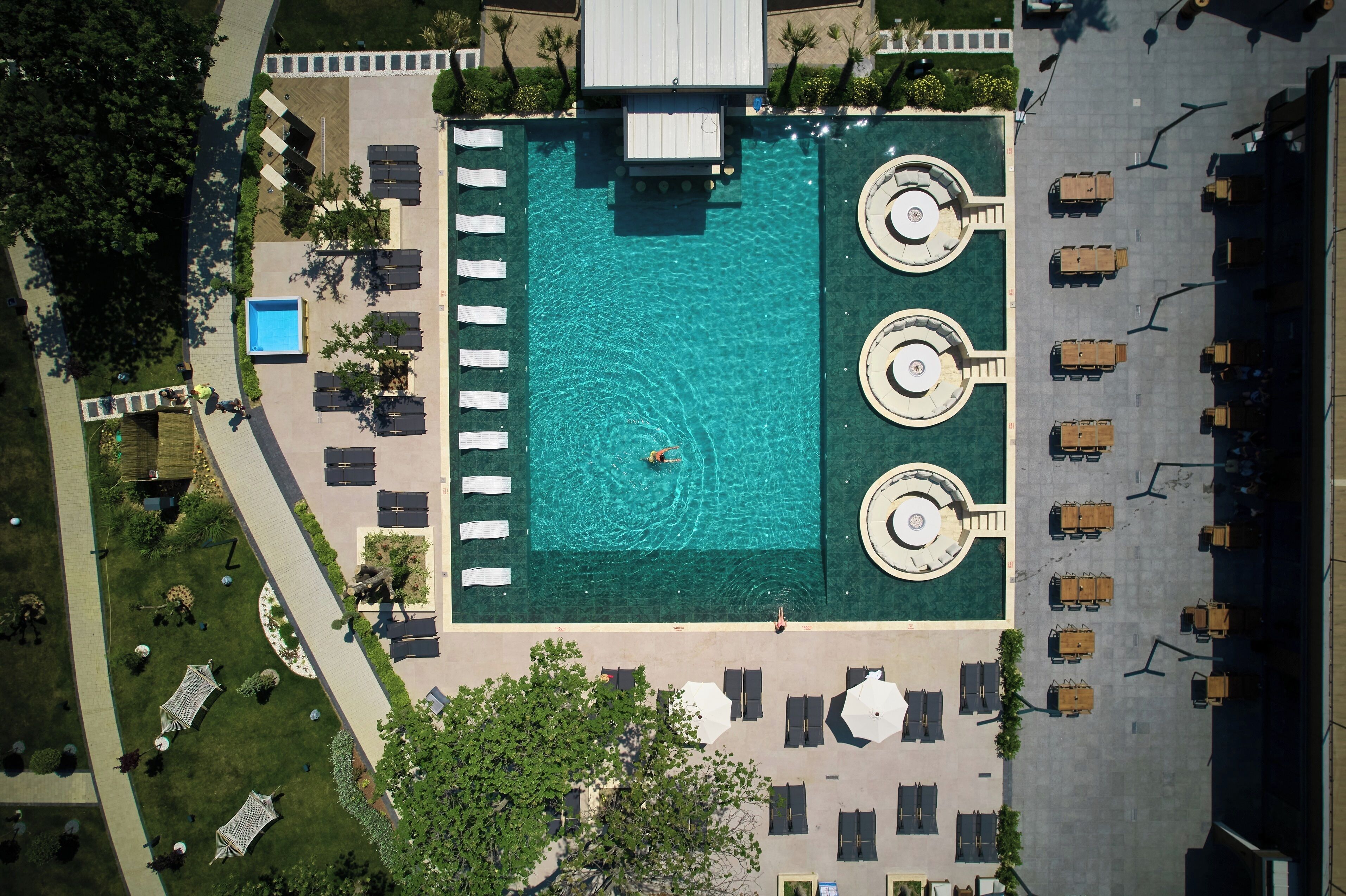 Vista aérea de un hotel con piscina central, múltiples tumbonas y un aparcamiento con varios vehículos.