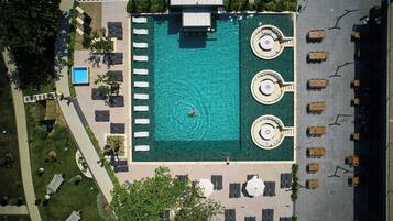 Vista aérea de un hotel con piscina central, múltiples tumbonas y un aparcamiento con varios vehículos.