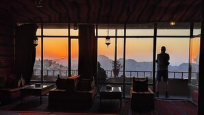 A room with large windows offering a view of the sunset and mountains. There are sofas and a table in the room.