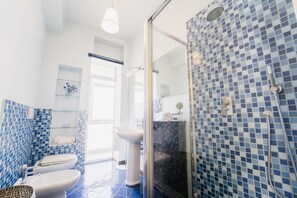 Un baño con ducha, inodoro y lavamanos, con azulejos de mosaico azules y puerta de vidrio.