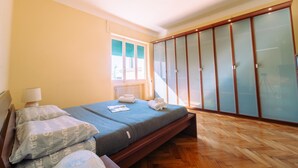 A bedroom with a bed, wooden flooring, a window with blinds, and a wardrobe with frosted glass doors. - Elegant Apartment in the Center by Wonderful Italy (Sanremo)
