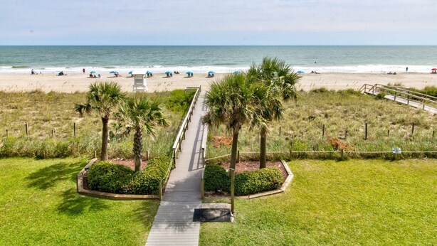 A pathway leading to a beach with palm trees and a view of the ocean. - 0311 Seaside Retreat by Atlantic Towers (Carolina Beach)