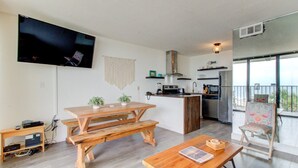 A modern kitchen with a large island, a dining area with wooden tables, and a balcony with a view. - 0311 Seaside Retreat by Atlantic Towers (Carolina Beach)