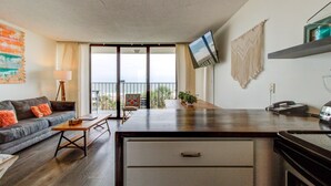 A modern living room with a sofa, coffee table, and a TV mounted on the wall. There is a balcony with a view of the ocean. - 0311 Seaside Retreat by Atlantic Towers (Carolina Beach)