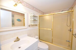 Un baño con lavamanos blanco, inodoro y ducha a ras de suelo con marco dorado.