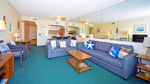 A living room with a sofa set, a coffee table, and a kitchen area visible through an open door. - Towers 402 2 Bedroom Condo by RedAwning (Ocean City)