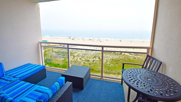A balcony with a view of the beach, a sofa, a table, and a chair. - Towers 402 2 Bedroom Condo by RedAwning (Ocean City)