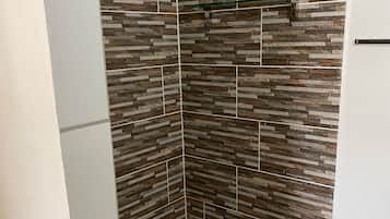 A shower with a stone tile wall and a white door.