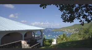Un bâtiment situé sur la côte, doté d’un toit bleu clair, d’un balcon et offrant une vue sur la mer et le paysage lointain.