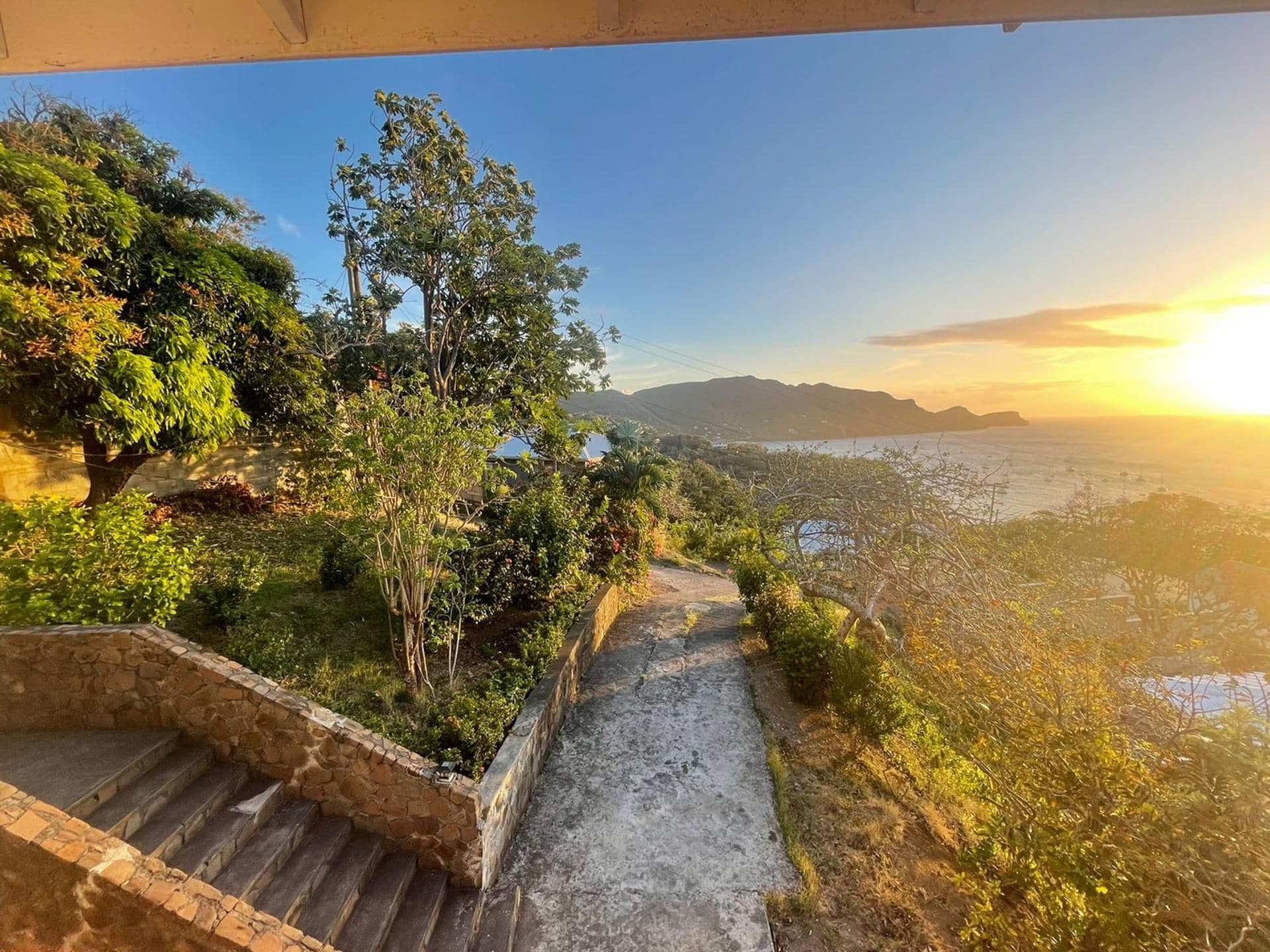A stone staircase leading to a scenic overlook with a view of the ocean and distant mountains during sunset.