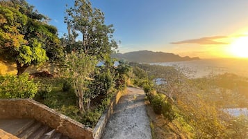 A stone staircase leading to a scenic overlook with a view of the ocean and distant mountains during sunset.