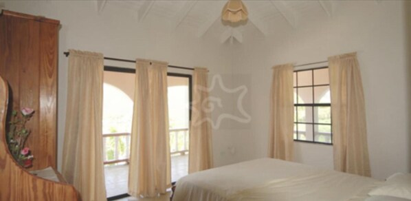 Un dormitorio con cama, dos ventanas con cortinas, un armario de madera y un ventilador de techo.