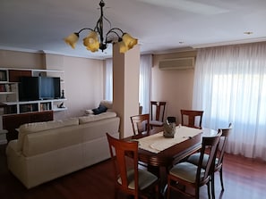 Un salon comprenant un canapé, une table à manger, des chaises, un téléviseur et des étagères.