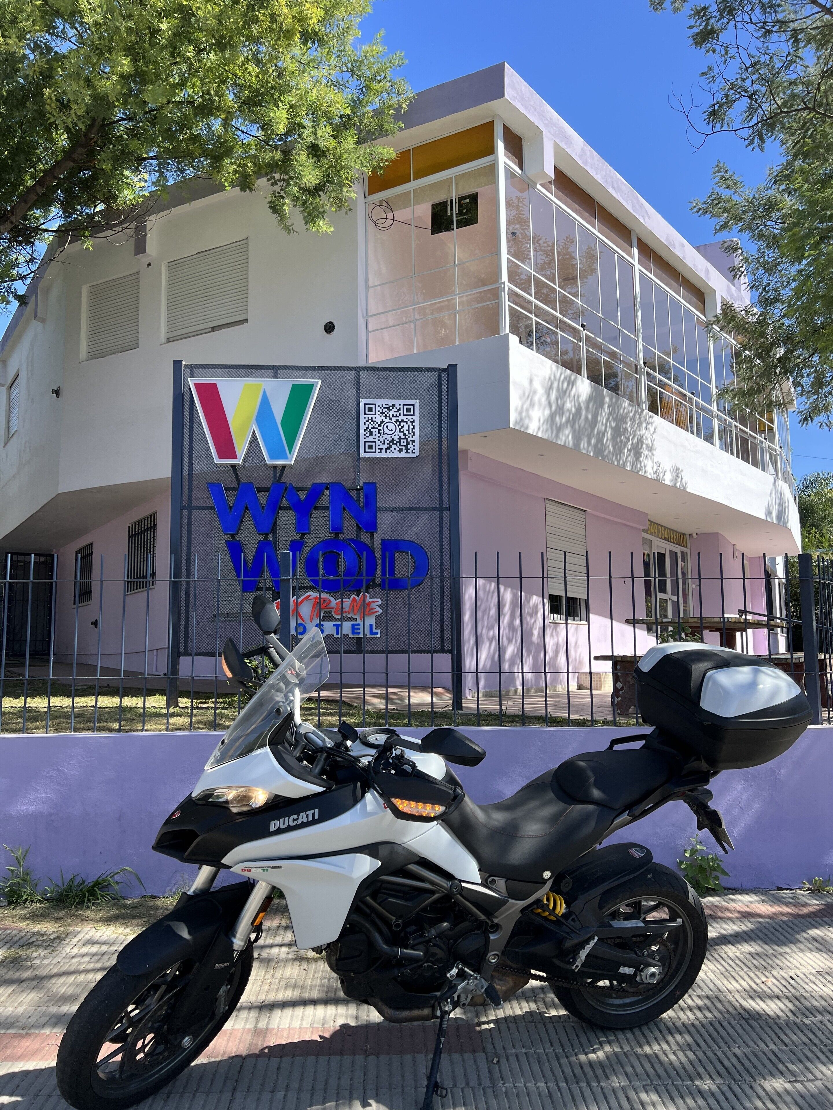Una motocicleta Ducati blanca estacionada frente a un edificio con un letrero que dice 'WYNN KREW HOTEL'.