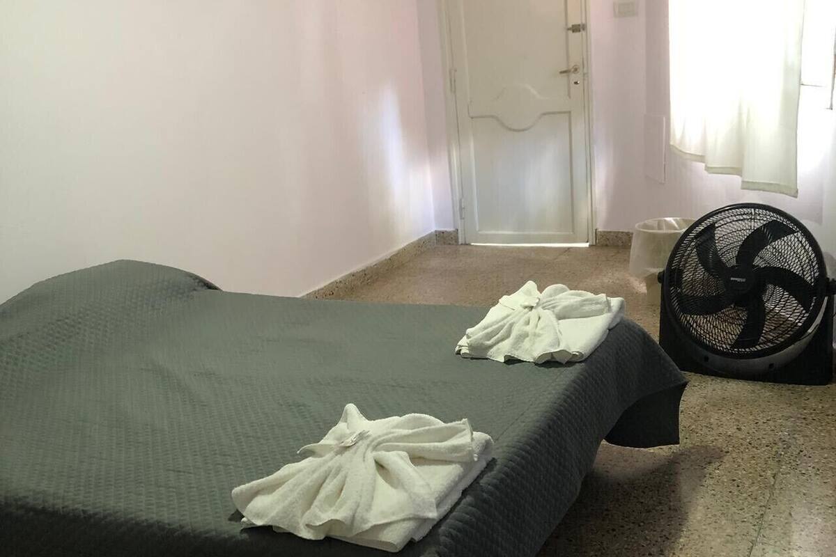 Une pièce avec un lit, un ventilateur et une porte.