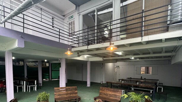 A spacious indoor area with multiple wooden benches and tables, some with potted plants. There are railings and a mezzanine level visible. - Hostel Wynwood Extreme (Villa Carlos Paz)