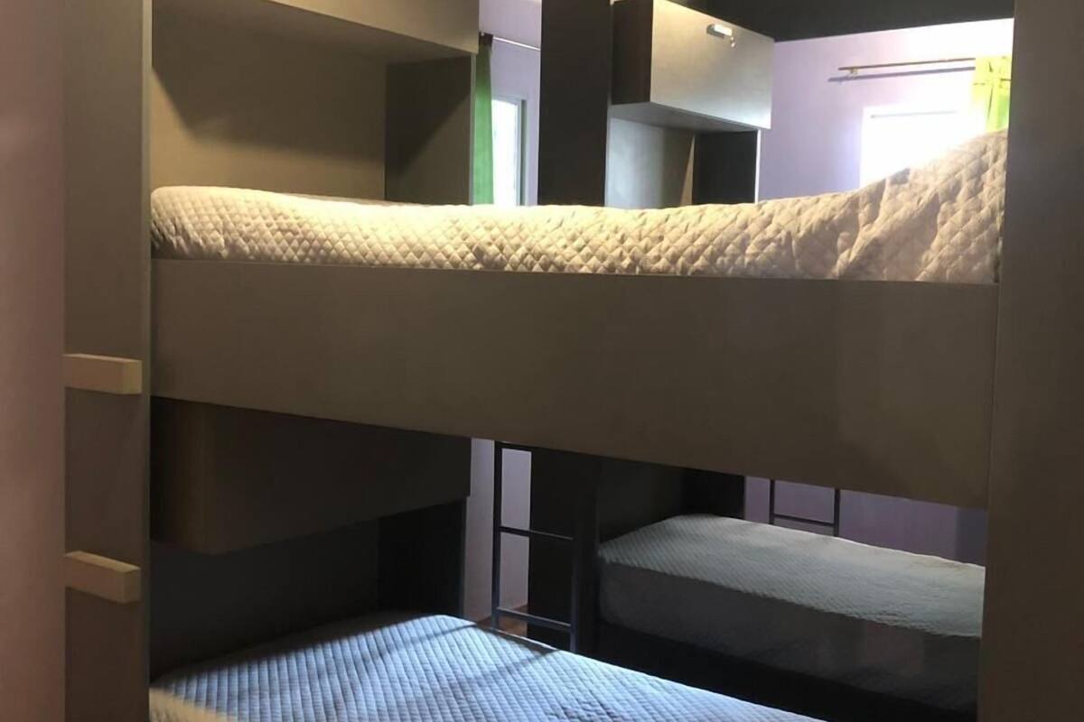Un lit superposé avec une échelle sur le côté gauche, une fenêtre donnant sur un paysage et une porte au fond.