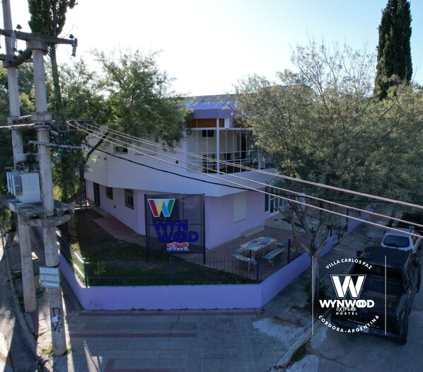 A modern building with a prominent 'WYN WOD' sign, a small outdoor seating area, and a parking space. - Hostel Wynwood Extreme (Villa Carlos Paz)