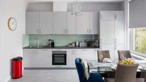 Une cuisine moderne avec des meubles blancs, un four noir et un coin repas comprenant une table et des chaises en verre.