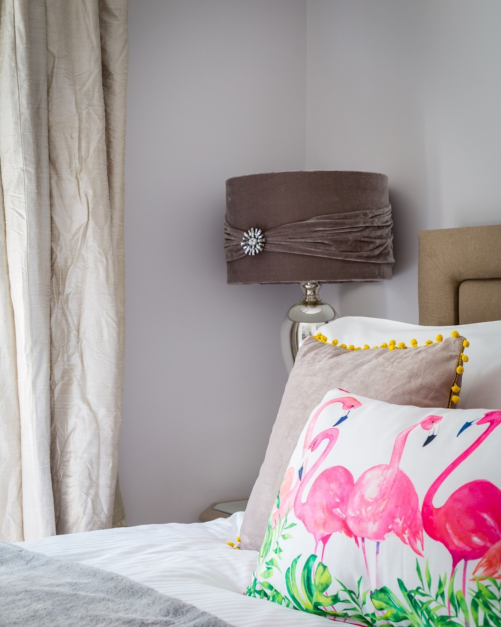 A neatly made bed with a white comforter and a pillow with flamingo designs.