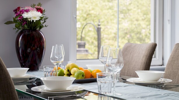 Une table à manger dressée avec des assiettes, des bols, des verres et un vase rempli de fleurs.