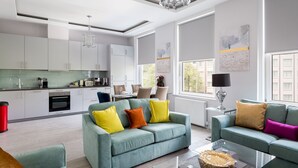 Un salon moderne avec un canapé de couleur turquoise, une table basse en verre et un coin repas comprenant une table et des chaises blanches.