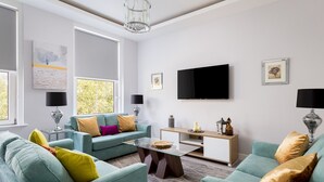Un salon moderne avec des canapés de couleur turquoise, une table basse en verre et un téléviseur à écran plat fixé au mur.