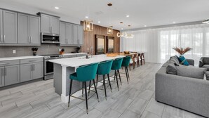 Une cuisine moderne avec des meubles gris, un plan de travail blanc et des tabourets de bar de couleur turquoise.