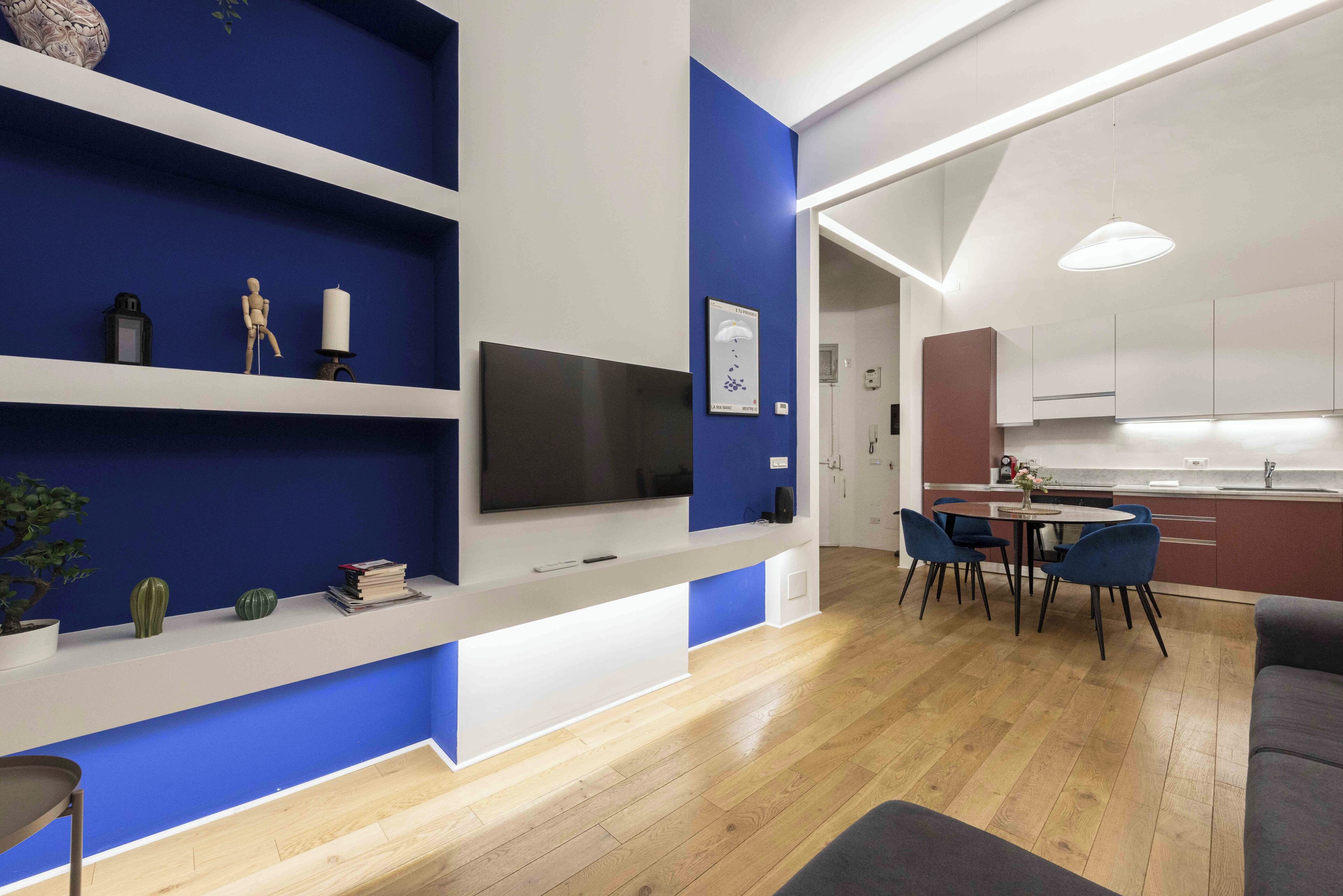 A modern living room with a TV, shelves, and a dining area with chairs.